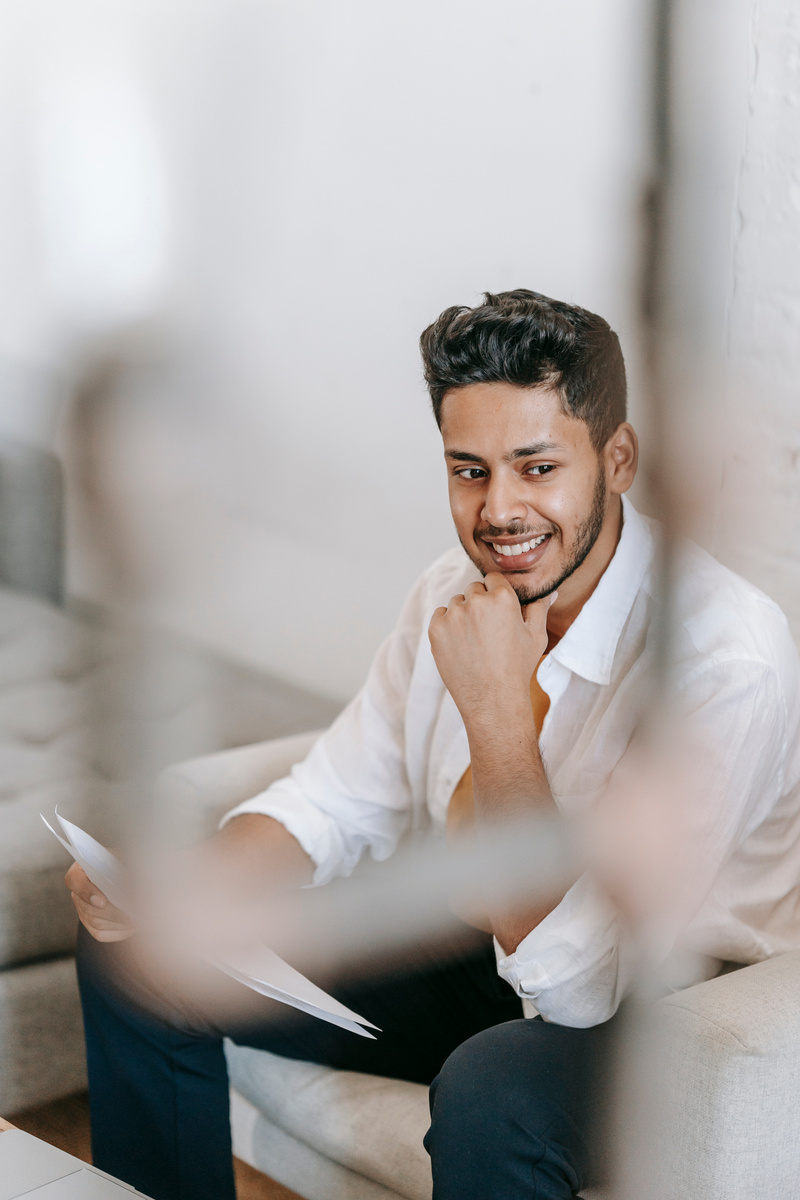 Smiling ethnic man reading documents on armchair